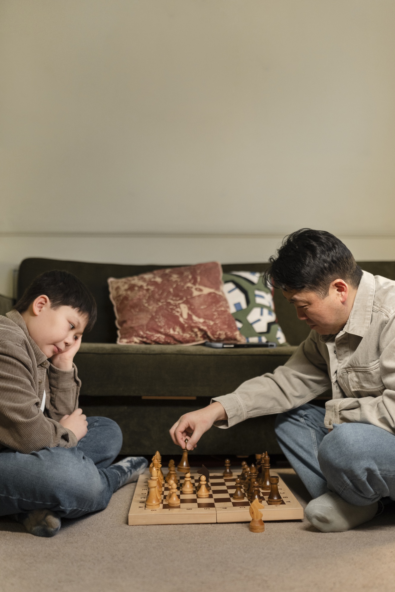 Pai e filho jogando xadrez acompanhados por um professor
